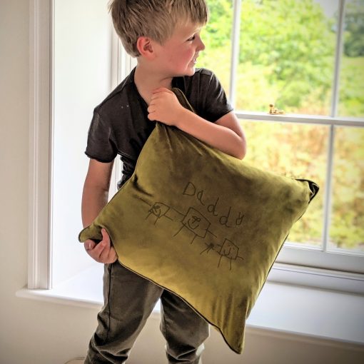 Child holding a velvet cushion with a bespoke engraving of child's artwork